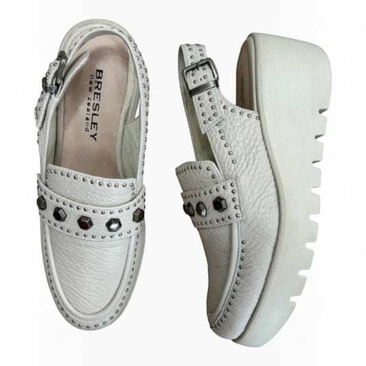 The Shoe Shop Peeps white leather wedge loafers featuring gunmetal stud detailing, a buckle strap, and a chunky sole.