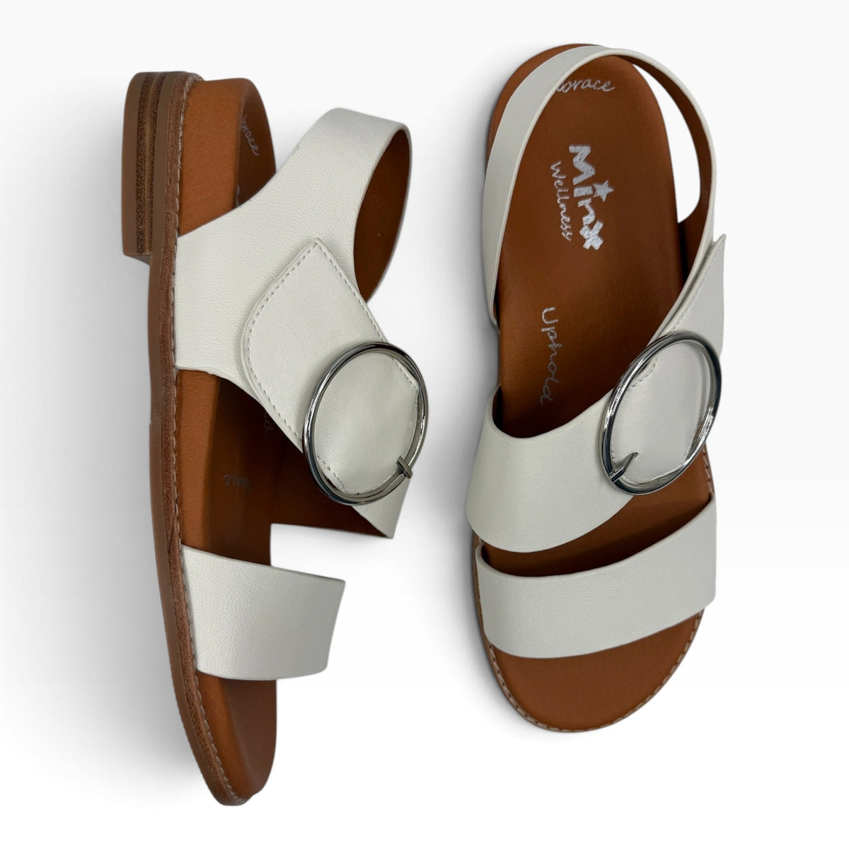 The Shoe Shop Willa white leather sandals featuring a large silver buckle and a comfortable brown flat sole