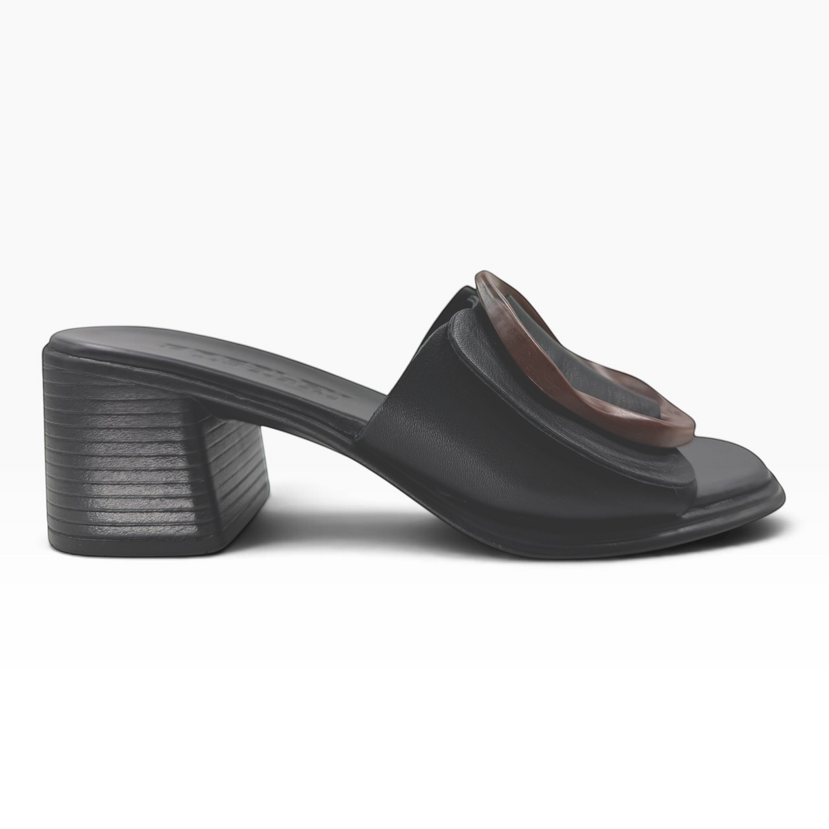 The Shoe Shop Panton Slide in black leather featuring a low block heel and a tortoiseshell-effect circular ornament.