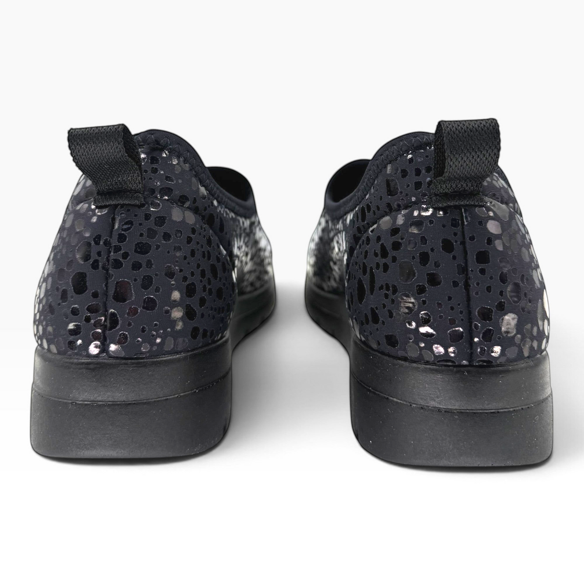 The Shoe Shop Florence slip-on shoes in black with a metallic spotted pattern, featuring a pull tab and flat sole.
