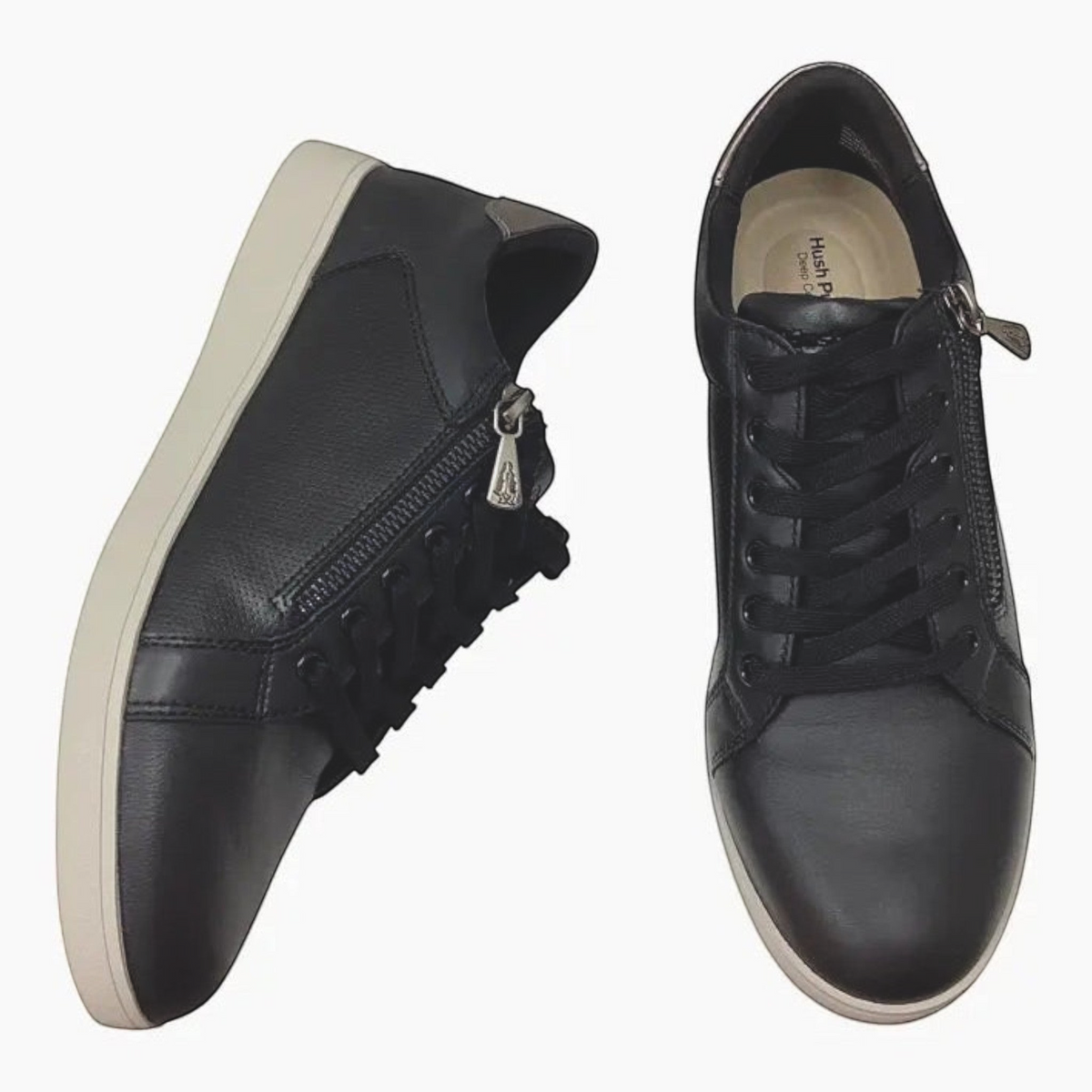 The Shoe Shop Hush Puppies Mimosa black leather sneakers with side zip, perforated panels, and gunmetal heel detail.