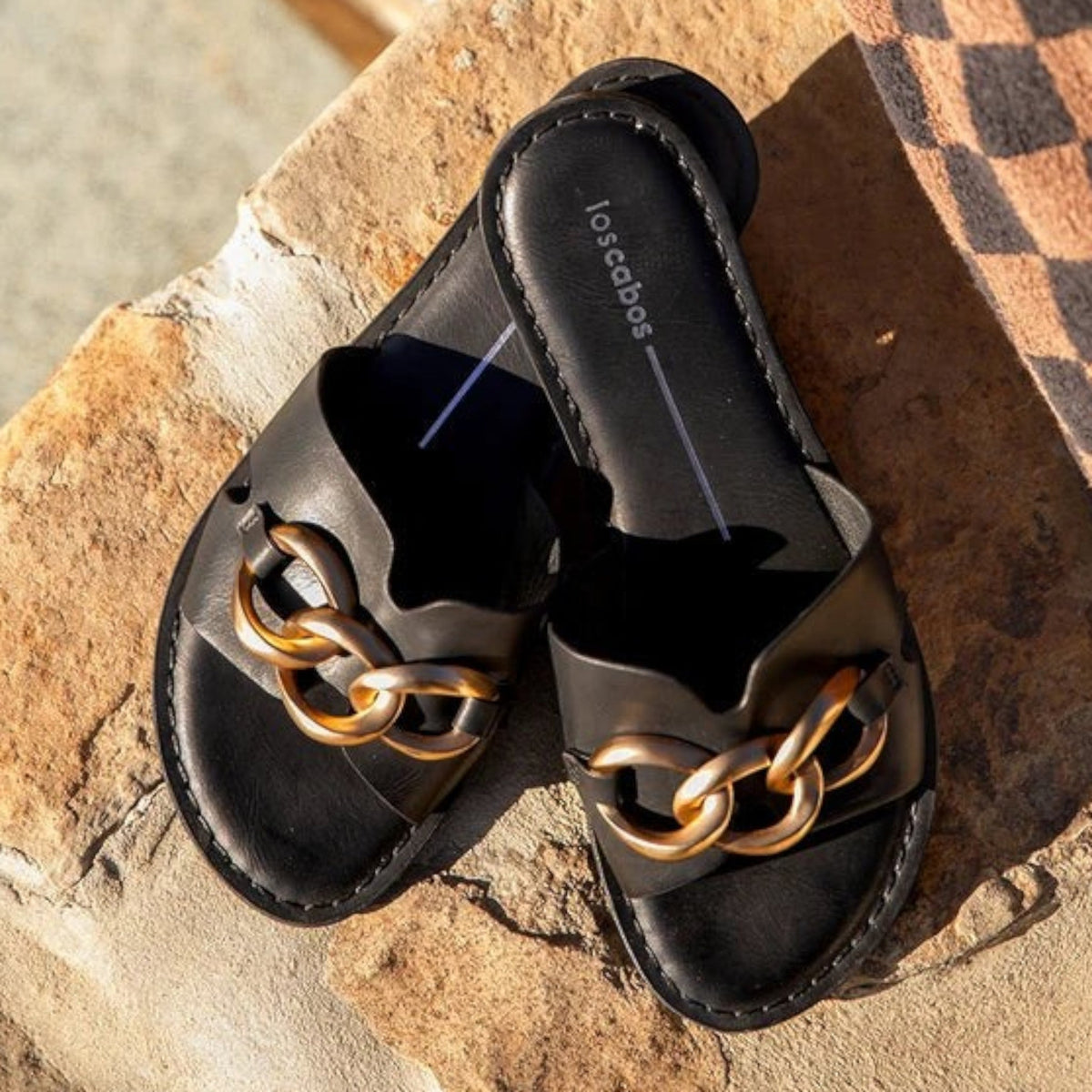 The Shoe Shop Maiz black slide sandals featuring a chunky gold-tone metallic chain detail on a flat sole