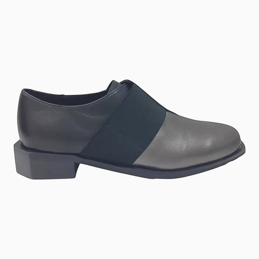 The Shoe Shop Raya flat shoe in pewter leather with a black elastic strap and low block heel, side view.