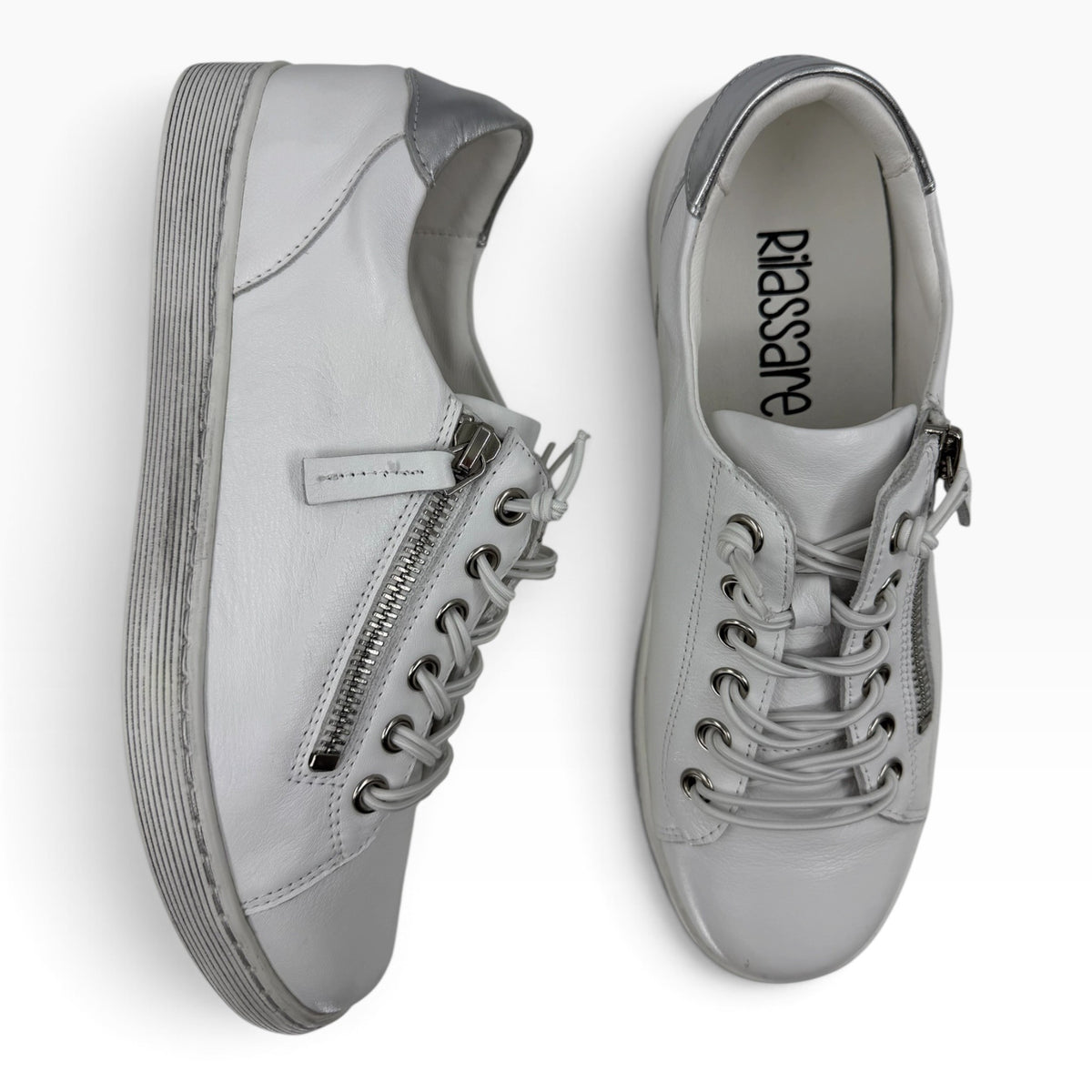 The Shoe Shop Rilassare Temi white leather sneakers with side zip, elastic laces, and silver heel detail.